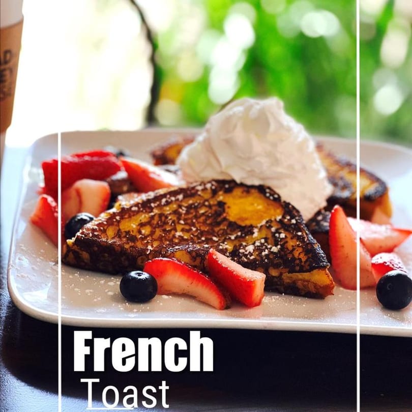 Golden French toast slices with whipped cream, strawberries, and blueberries on a white plate.