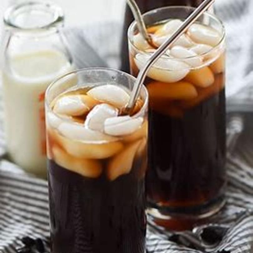 Two glasses of iced coffee with milk and ice, with a bottle of milk in the background.
