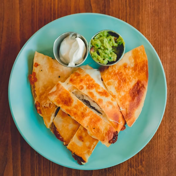 Golden-brown quesadilla slices with melted cheese, served with guacamole and sour cream on a blue plate.