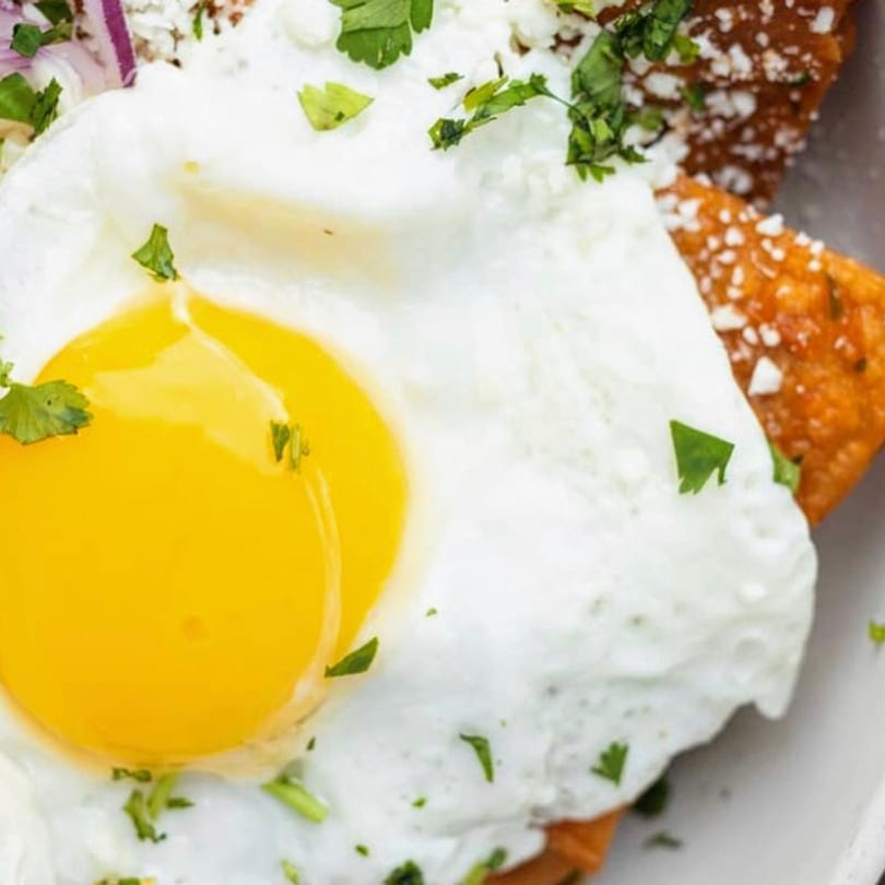 Close-up of a fried egg with a bright yellow yolk, cilantro, and crumbled cheese over chilaquiles.