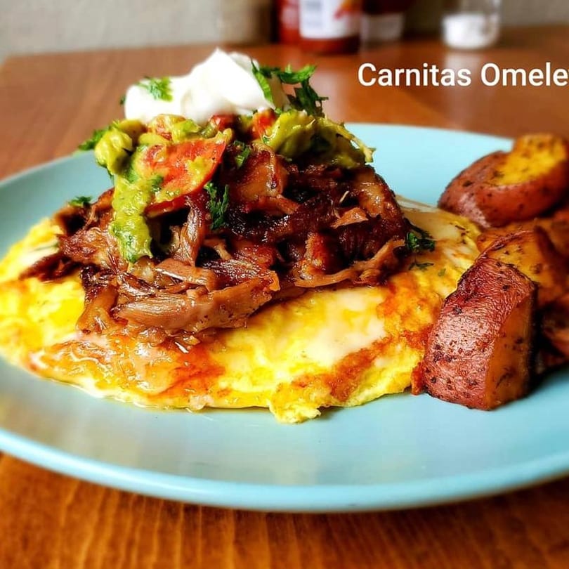 Carnitas omelet topped with guacamole, sour cream, and cilantro, served with roasted potatoes.
