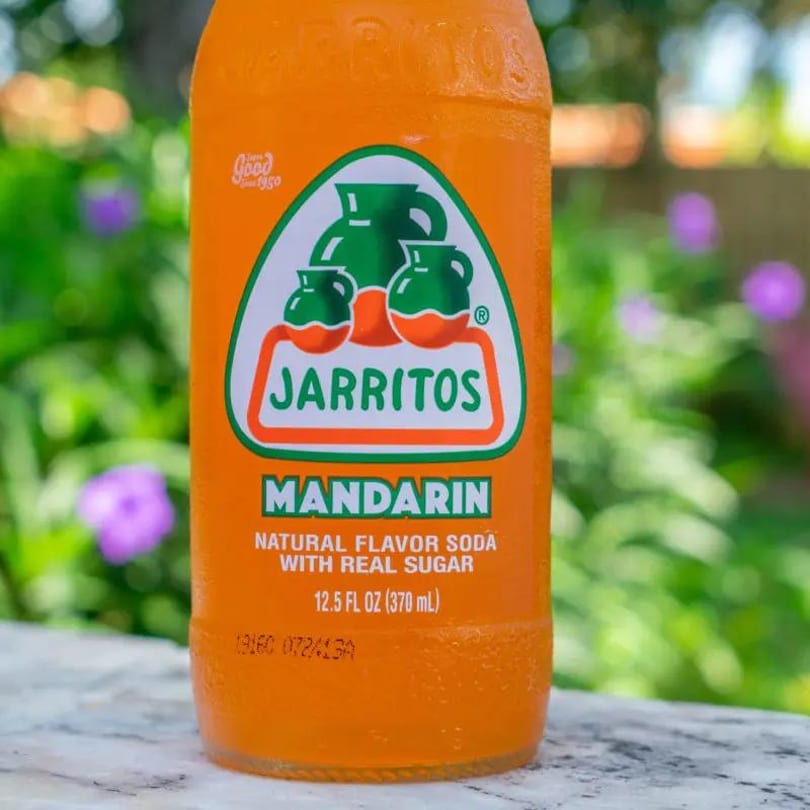 Close-up of a Jarritos Mandarin soda bottle with a green and orange label, outdoors.
