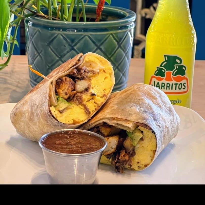 Two breakfast burritos, one cut in half, with a side of salsa and a Jarritos soda.
